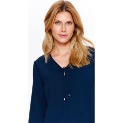BLUZKA DAMSKA Z WIĄZANIEM Z OZDOBNĄ KOŃCÓWKĄ. Niebieskie bluzki damskie Top Secret, bez wzorów, z jeansu, eleganckie, z dekoltem w serek, bez rękawów. W wyprzedaży za 39,99 zł.