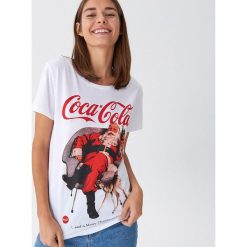 Koszulka Coca-Cola - Biały. Białe koszulki damskie House, s, bez wzorów, bez kołnierzyka, bez rękawów. Za 49,99 zł.
