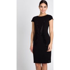 Czarna sukienka z błyszczącym wzorem QUIOSQUE. Czarne sukienki mini marki QUIOSQUE, na imprezę, z tkaniny, eleganckie, z kopertowym dekoltem, dopasowane. W wyprzedaży za 149,99 zł.