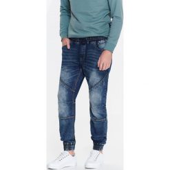 SPODNIE MĘSKIE TYPU JOGGER Z DZIANINY IMITUJĄCEJ JEANS. Niebieskie jeansy męskie z dziurami marki Top Secret, na lato, m, z jeansu. W wyprzedaży za 119,99 zł.