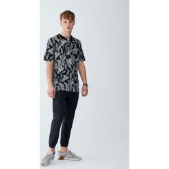 Koszulka polo z tropikalnym nadrukiem liści. Czarne koszulki męskie Pull&Bear, m, z nadrukiem, z krótkim rękawem. Za 59,90 zł.