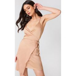 Linn Ahlborg x NA-KD Kopertowa sukienka z satyny - Nude. Szare sukienki damskie Linn Ahlborg x NA-KD, bez wzorów, z satyny, bez kołnierzyka, bez rękawów, kopertowe. W wyprzedaży za 66,97 zł.