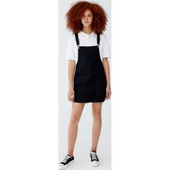 Jeansowa sukienka ogrodniczka z niewykończonym dołem. Czarne sukienki damskie marki Pull&Bear, bez wzorów, z jeansu, bez kołnierzyka, bez rękawów. Za 89,90 zł.