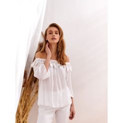 Bluzka z koronkowym zdobieniem przy dekolcie. Białe bluzki damskie Top Secret, w koronkowe wzory, z koronki, eleganckie, bez kołnierzyka, bez rękawów. W wyprzedaży za 39,99 zł.