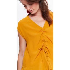 Bluzka tkaninowa z ozdobnym wiązaniem. Żółte bluzki damskie Top Secret, bez wzorów, z tkaniny, eleganckie, z dekoltem w serek, bez rękawów. W wyprzedaży za 19,99 zł.