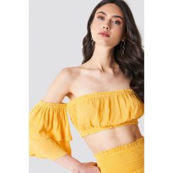 Linn Ahlborg x NA-KD Top z krepy z odkrytymi ramionami - Yellow. Żółte topy damskie marki Linn Ahlborg x NA-KD, bez wzorów, z falbankami. W wyprzedaży za 40,38 zł.