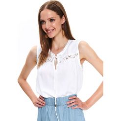 Bluzka bez rękawów z koronkową aplikacją. Białe bluzki damskie Top Secret, w koronkowe wzory, z tkaniny, bez kołnierzyka, bez rękawów. W wyprzedaży za 39,99 zł.