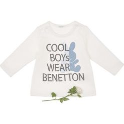 Bluza w kolorze kremowym. Białe bluzy niemowlęce Benetton Kids, z nadrukiem, z bawełny, bez rękawów, bez kaptura. W wyprzedaży za 32,95 zł.