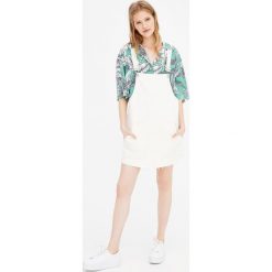 Jeansowa sukienka ogrodniczka z niewykończonym dołem. Białe sukienki damskie z falbanami marki Pull&Bear, z jeansu. Za 89,90 zł.
