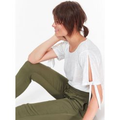 T-shirt damski z dzianiny z błyszczącą nitką, z rozcięciami i wiązaniem na rękawach. Białe t-shirty damskie Top Secret, bez wzorów, z bawełny, eleganckie, bez kołnierzyka. W wyprzedaży za 29,99 zł.