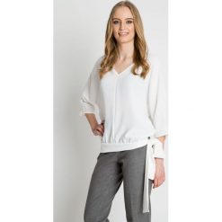 Bluzka w kolorze ecru z ozdobnym wiązaniem u dołu BIALCON. Szare bluzki damskie BIALCON, bez wzorów, eleganckie, z dekoltem w serek, bez rękawów. W wyprzedaży za 125,00 zł.