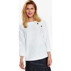 Bluzka damska z ozdobną przypinką. Białe bluzki damskie Top Secret, z aplikacjami, z dzianiny, eleganckie, z dekoltem w serek, bez rękawów. W wyprzedaży za 69,99 zł.