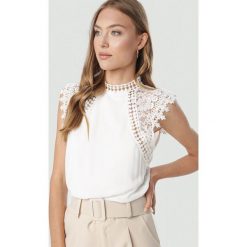 Biała Bluzka Themigeia. Białe bluzki damskie Born2be, uniwersalny, bez wzorów, bez kołnierzyka, bez rękawów. W wyprzedaży za 89,99 zł.