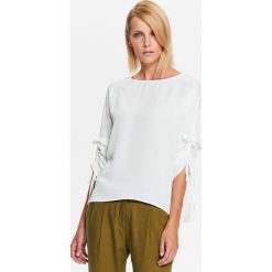 Bluzka gładka ze ściądanymi tasiemkami na rękawach. Białe bluzki damskie Top Secret, s, bez wzorów, eleganckie, z falbankami, bez rękawów. W wyprzedaży za 39,99 zł.
